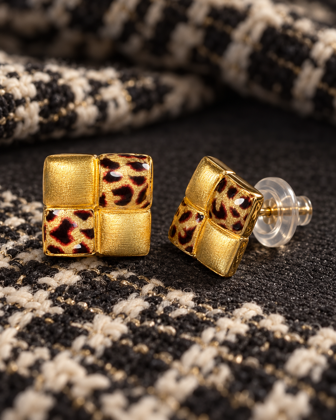 A pair of square leopard checkerboard stud earrings on black and ivory fabric, with a straight post and transparent push back visible.